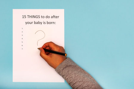 Caption 15 things to do after your baby is born. White A4 sheet on a blue background with a question markの写真素材