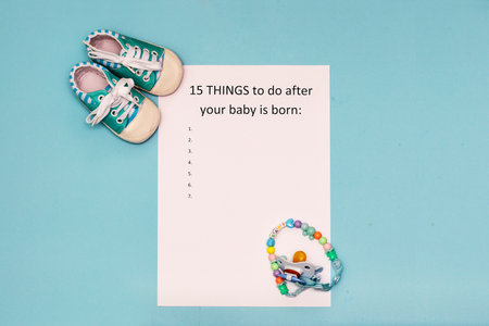 Caption 15 things to do after your baby is born. White A4 sheet on blue background next to baby blue booties and pacifier holderの写真素材