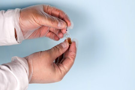 Male hand in a transparent medical nitrile glove holds a vial of medication. Medicine concept.