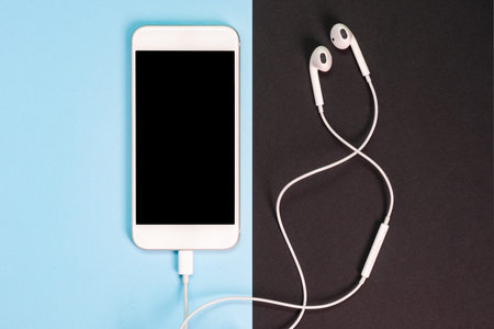 White smartphone on the blue and black background with headphones. View from above