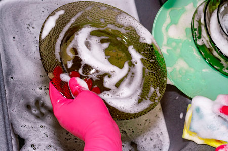 The process of washing plates in the sink, hands and plates closeup. Detergent foams. Cleaning