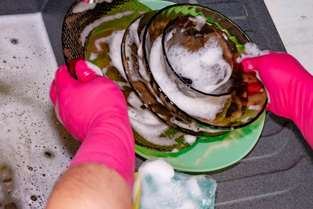 The process of washing plates in the sink, hands and plates closeup. Detergent foams. Cleaningの写真素材