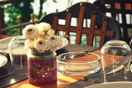 Served table in a summer cafe. The sea in the background. Wooden furniture, white flowers