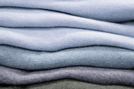 Warm clothing neatly folded on a store shelf. Sweatshirts, sweaters, jumpers, cardigans, hoodies, bobmers with piles on the shelf. Clothes storage. Size rangeの写真素材