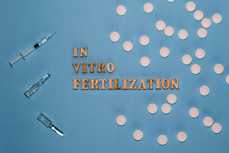 The inscription In Vitro Fertilization is in wooden letters on a blue background. In vitro injection pen, tablet and ampoule. A syringe with a thin huge. IVF concept.の写真素材