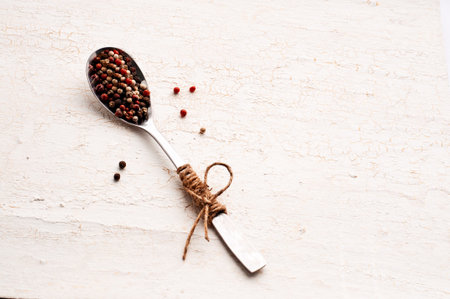 Multi-colored pepper seeds in a spoon with a handle drawn by a scourge. Bow from the scourge. Light background. Seasonings and cookingの写真素材