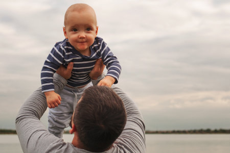 The child is in the arms of his father. A child against the background of the sky in the hands of dad. Happy moments of lifeの写真素材