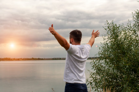 Handsome guy on the lake. Hands up. Liberty. Victory