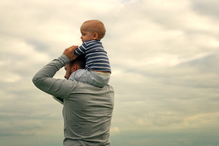 Baby in the arms of dad. Walk near the water. Baby and dad against the skyの写真素材