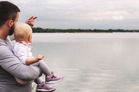 A child in the arms of a man. Walk near the water. Baby and dad against the skyの写真素材