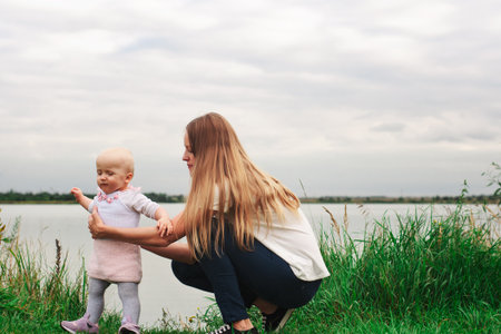 A girl learns to walk with her mother in nature. Mom and daughter, learning and development. The first steps of the child. Happy moments of lifeの写真素材