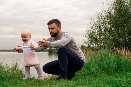Dad teaches daughter to walk, park, nature. Walk on the grass. Father and daughter. First steps
