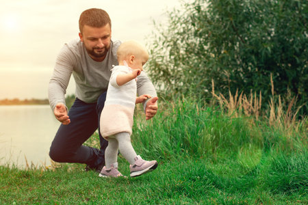 Dad teaches daughter to walk, park, nature. Walk on the grass. Father and daughter. First stepsの写真素材