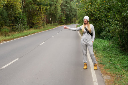 A young and beautiful girl votes on the road. Autumn road. Catch a car on an empty road....