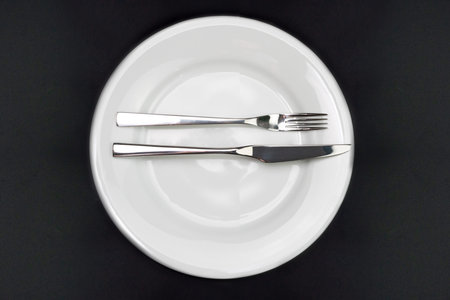 Table setting. Empty plate, knife and fork on a black background. The fork and knife lie on a plate...