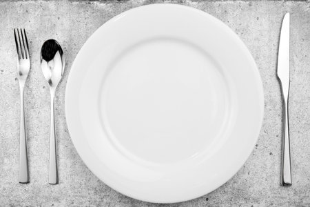 Table setting. Empty plate, knife, fork and a spoon on a light concrete background. Top view and flat lay with copy spaceの写真素材