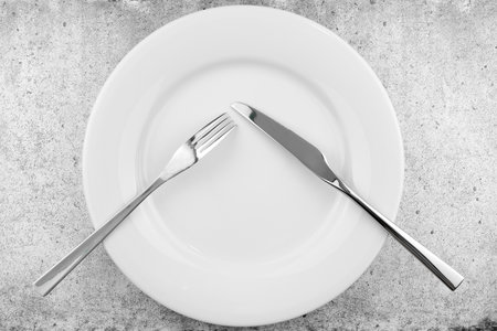 Table setting. Empty plate, knife and fork on a light concrete background. Fork and knife are on the plate, pause in food. Top view and flat lay with copy space.の写真素材