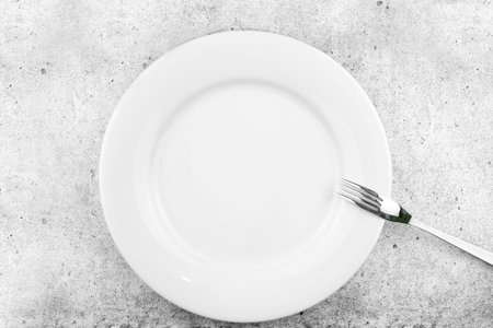 Table setting. Empty plate, fork on a light concrete background. A fork lies on a plate, a pause in food. Top view and flat lay with copy space.の写真素材
