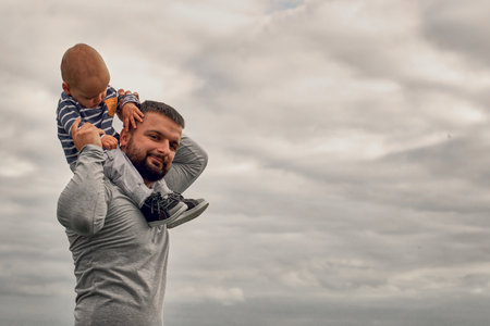 A child on his fathers neck. Walk near the water. Baby and dad against the sky.の写真素材