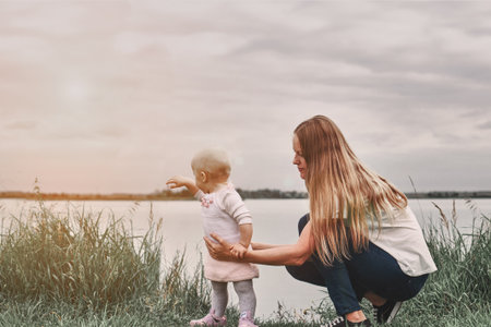 A girl learns to walk with her mother in nature. Mom and daughter, learning and development. The first steps of the child. Happy moments of life.の写真素材