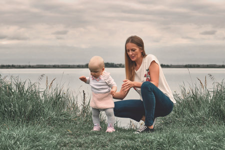 A girl learns to walk with her mother in nature. Mom and daughter, learning and development. The first steps of the child. Happy moments of life.の写真素材