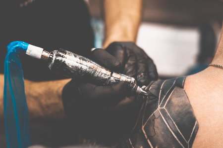 Tattoo salon. The tattoo master is tattooing a man on his shoulder. Tattoo machine, safety and hygiene at work. Close-up, tinted, tattooist.の写真素材