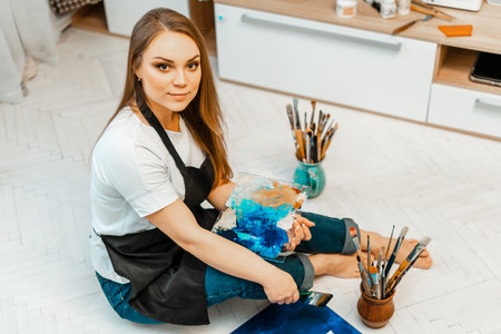 Art, the work of the artist. Young beautiful girl artist paints a picture. Workshop of the artist. The process of creativity. Drawing and paint. Inventory of the artist. Close-up.の写真素材