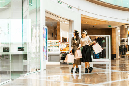 Shopping and entertainment, mall inside. Two beautiful girls with paper bags at the mall. The joy of consumption, Gift shopping, holidayの写真素材