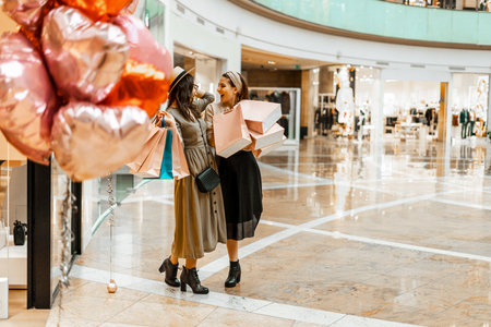 Shopping and entertainment, mall inside. Two beautiful girls with paper bags in the mall, heart-shaped balloons. The joy of consumption, Gift shopping, holiday.の写真素材