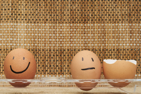 Chicken eggs in an egg holder. Full tray of eggs. Half an egg, egg yolk, shell. Emotion and facial expression painted on eggsの写真素材