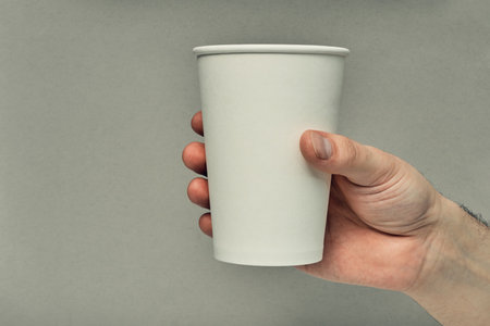 Paper cup in hand on a colored background. Eco-friendly materials in a coffee shop, biodegradable disposable tableware. Close up.の写真素材