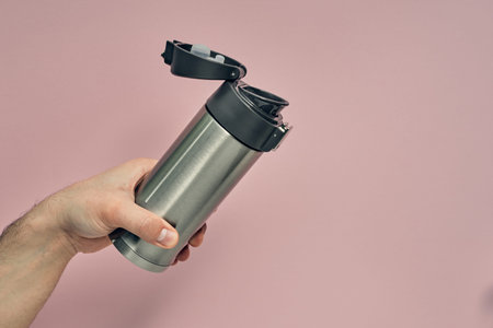 Metal mug flask in hand on a colored background. Hot drinks on the go. Thermo mug.の写真素材