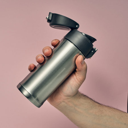 Metal mug flask in hand on a colored background. Hot drinks on the go. Thermo mug.の写真素材