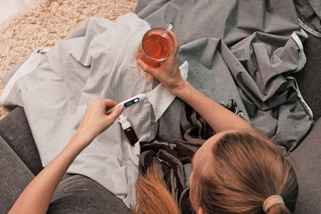 The girl is sick at home. Sitting on a couch, wrapped in a blanket, a scarf around his neck. Drinks...