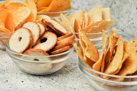 Potato and corn chips, snacks, crackers in transparent glass plates and sauces. Mix of snacks