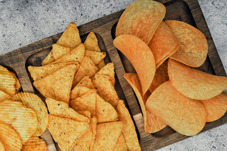 Chips, snacks and crackers on a wooden board. Fast food.