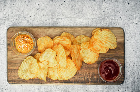 Fluted potato chips on a wooden board with sauce. Snack, ready meal menu, junk food. Close up.の写真素材