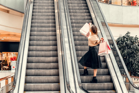 Two girls on an escalator in a shopping center. In the hands of paper bags. Shopping, leisure and entertainment.の写真素材
