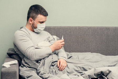 Disease. Cheer at home. A young man is sick, is treated at home. Blows her nose into a napkin, runny nose. Infection, epidemic, bacillus carrier.の写真素材