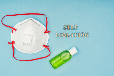 Coronavirus, Covid-19. Inscription self-isolation, a protective mask, an antiseptic and a dispenser for living soap on a blue background. Self-isolation and quarantine, personal protective equipment.の写真素材