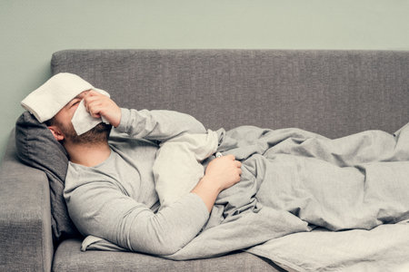 Disease. Cheer at home. A young man is sick, is treated at home. Blows her nose into a napkin, runny nose. Infection, epidemic, bacillus carrier.の写真素材