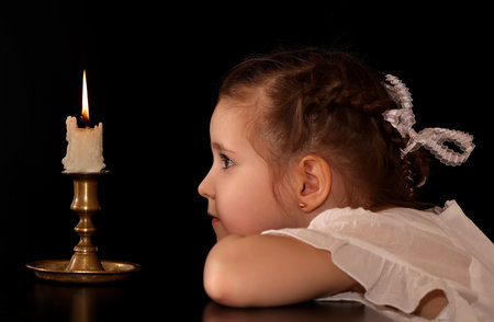 Portrait of a Girl 4-5-6 years, looking at the burning candle isolated on black background.の写真素材