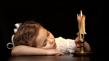 Portrait of a Girl 4-5-6 years, looking at the burning candle isolated on black background.の写真素材
