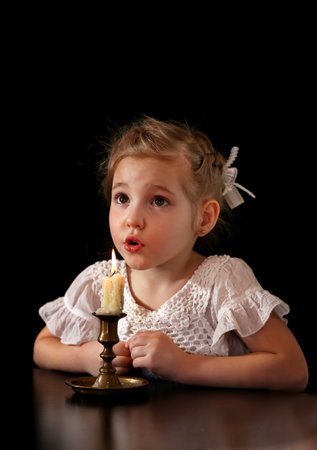 Portrait of a Girl 4-5-6 years, looking at the burning candle isolated on black background.の写真素材