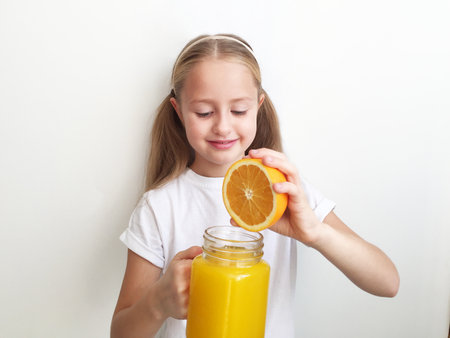 A girl holding a fresh orange in a cookie. girl stands on a white background. surprisedの写真素材