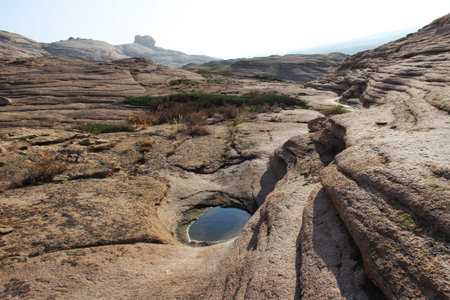 Volcanic layered mountains in the Bektau-Ata tract rise in layers, in front of a small puddle of water, green low bushes, slopes in the distance, summer, sunnyの写真素材