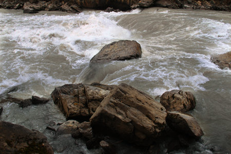 Large stones in a turbid river in Altai, white foam in the stream of water, close-up