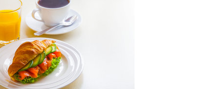 croissant sandwich with salmon and avocado, coffee and orange juice on a white backgroundの写真素材