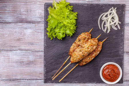 Lulya-kebab. Shish kebab on a stick, minced meat. Traditional Caucasian dish. On a cutting board, with green salad, ketchup, spices.の写真素材