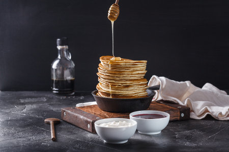 Pancakes with honey in a cast-iron frying pan on a black background, horizontal, copyspaceの写真素材